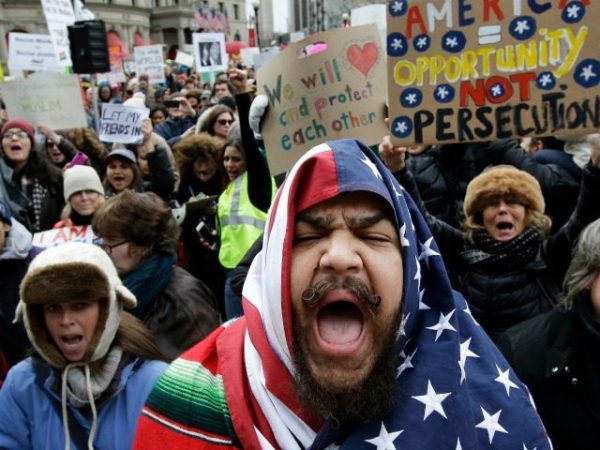Izzy Berdan, of Boston, center, wears an American flags as he chants slogans with other demonstrators during a rally against President Trump's order that restricts travel to the U.S., Sunday, Jan. 29, 2017, in Boston. Trump signed an executive order Friday, Jan. 27, 2017 that bans legal U.S. residents and visa-holders from seven Muslim-majority nations from entering the U.S. for 90 days and puts an indefinite hold on a program resettling Syrian refugees. (AP Photo/Steven Senne)